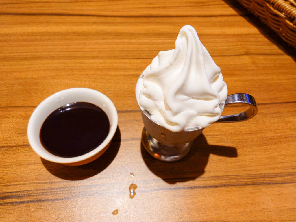 びっくりドンキー厚木妻田店のチョコソースのミニソフト。取っ手のついた金属のカップに入り、横にチョコソースの入った小さな器が置かれている